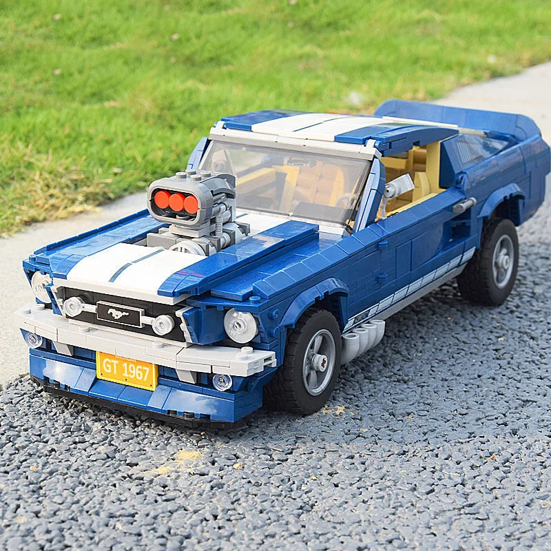 lego alternate builds 1960s Ford Mustang model with a supercharger, white racing stripes, GT 1967 license plate, and realistic details, displayed on a paved outdoor surface with grass in the background.